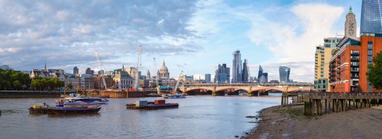 Panoramic view of the River Thames in London, showing boats, the Blackfriars Bridge, and modern city buildings under a partly cloudy sky.